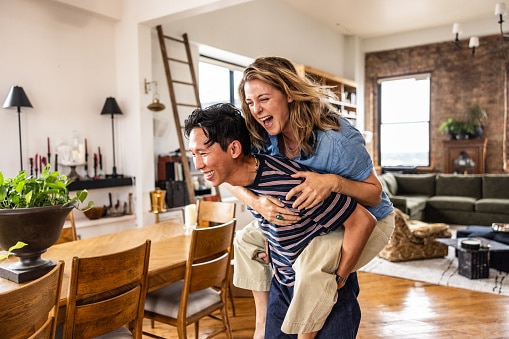Young man giving girlfriend a piggyback ride in spacious loft