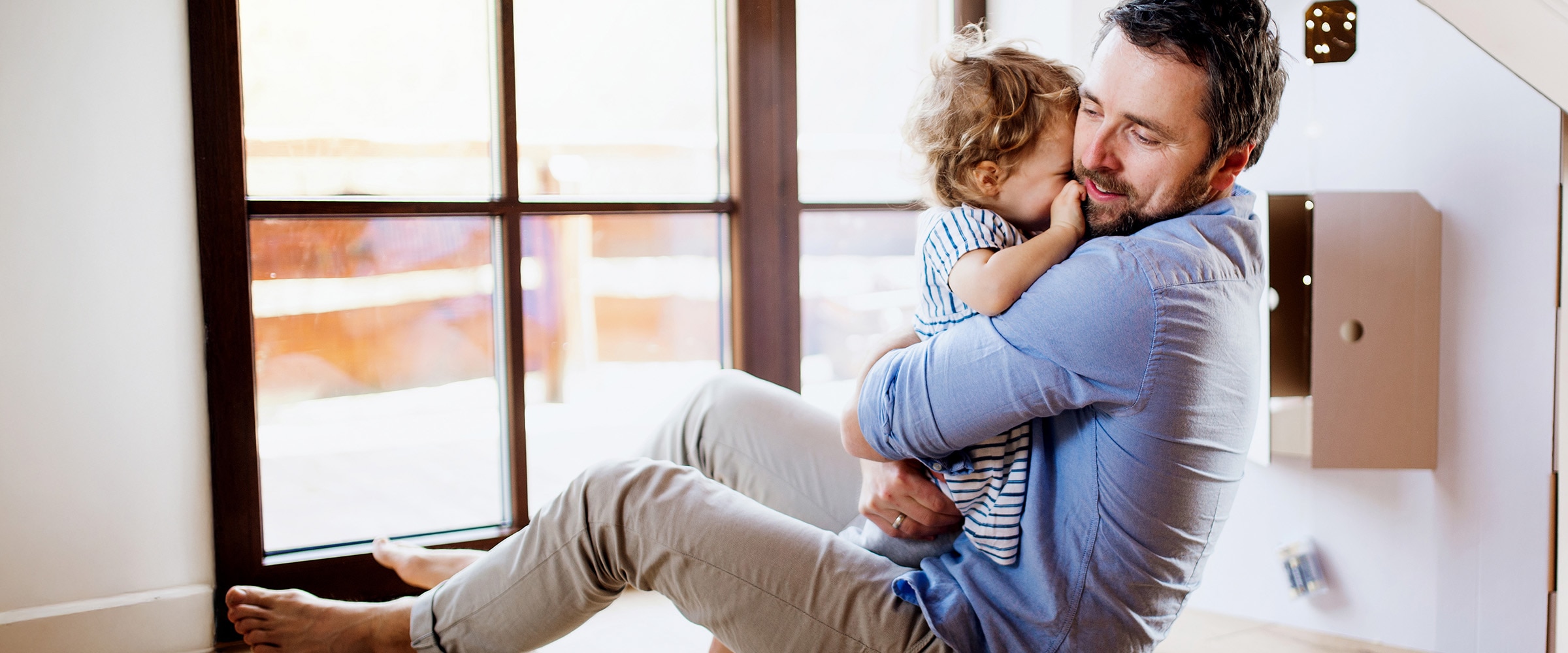 Photo of dad holding child close to this chest near window.