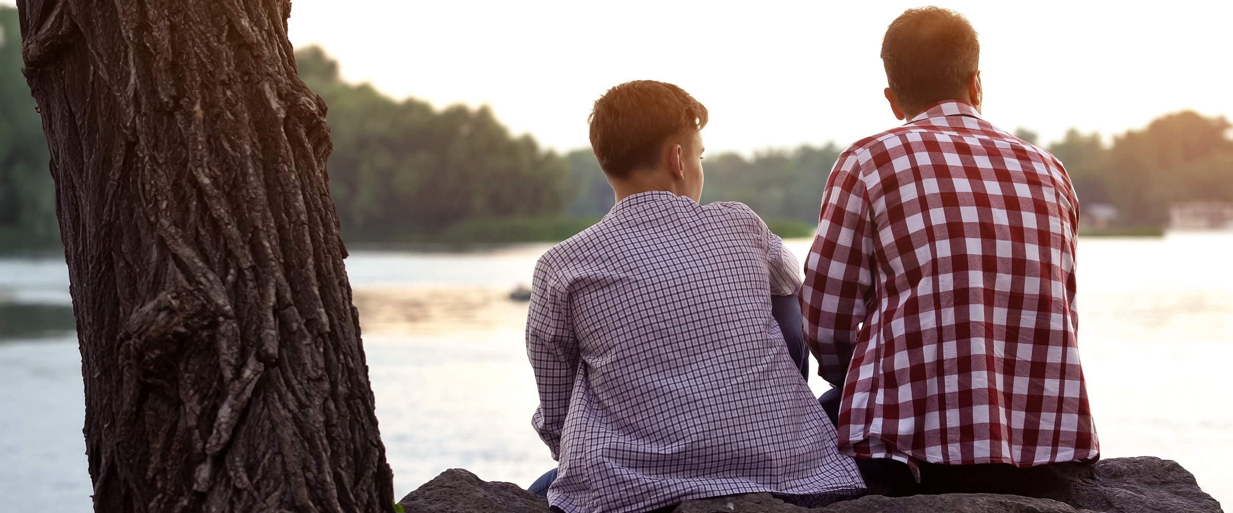 Photo of the backs of a father and son sitting on a dock.