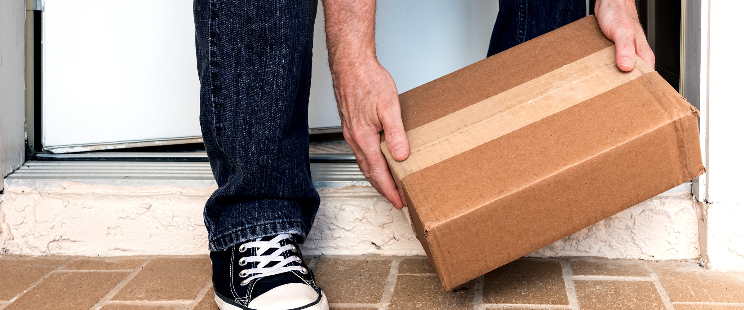 Photo of hands picking up a package at a doorstep.