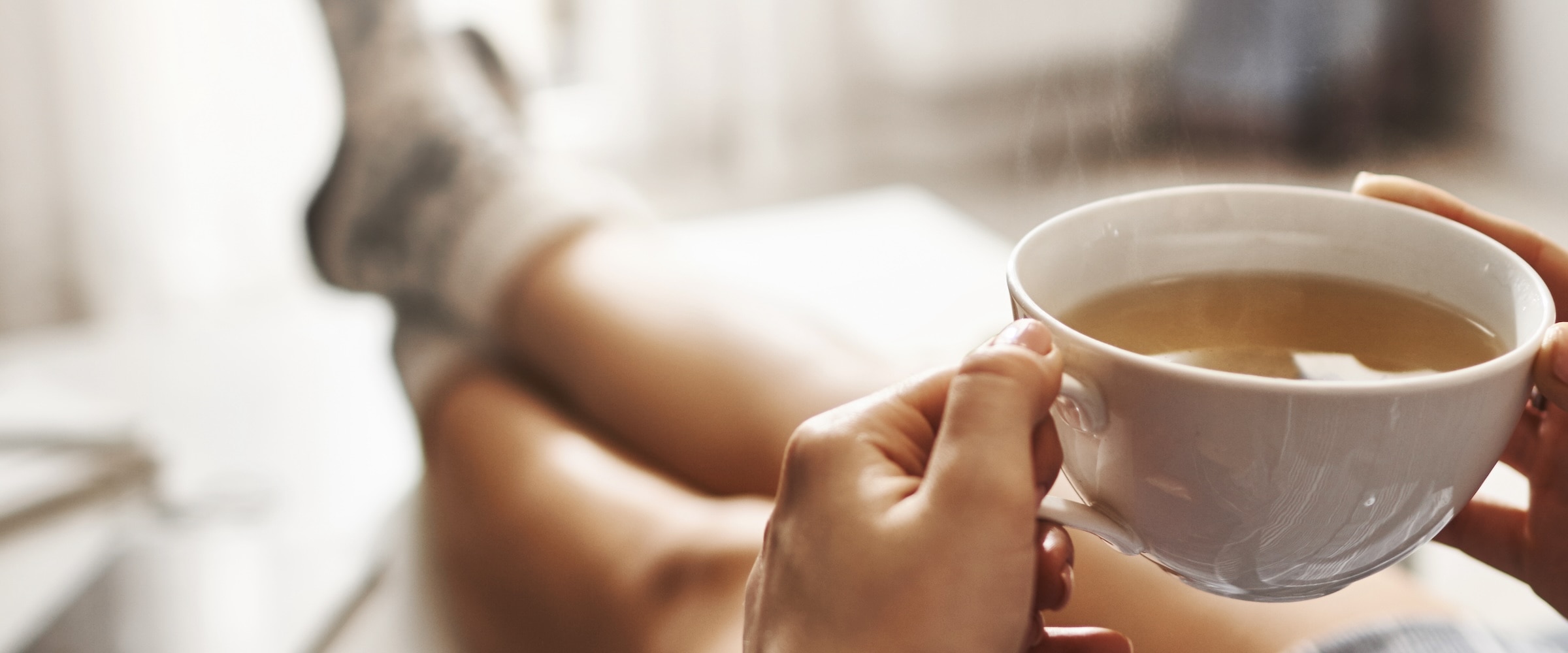 Photo of feet propped up on ottoman and hands holding a cup of coffee.