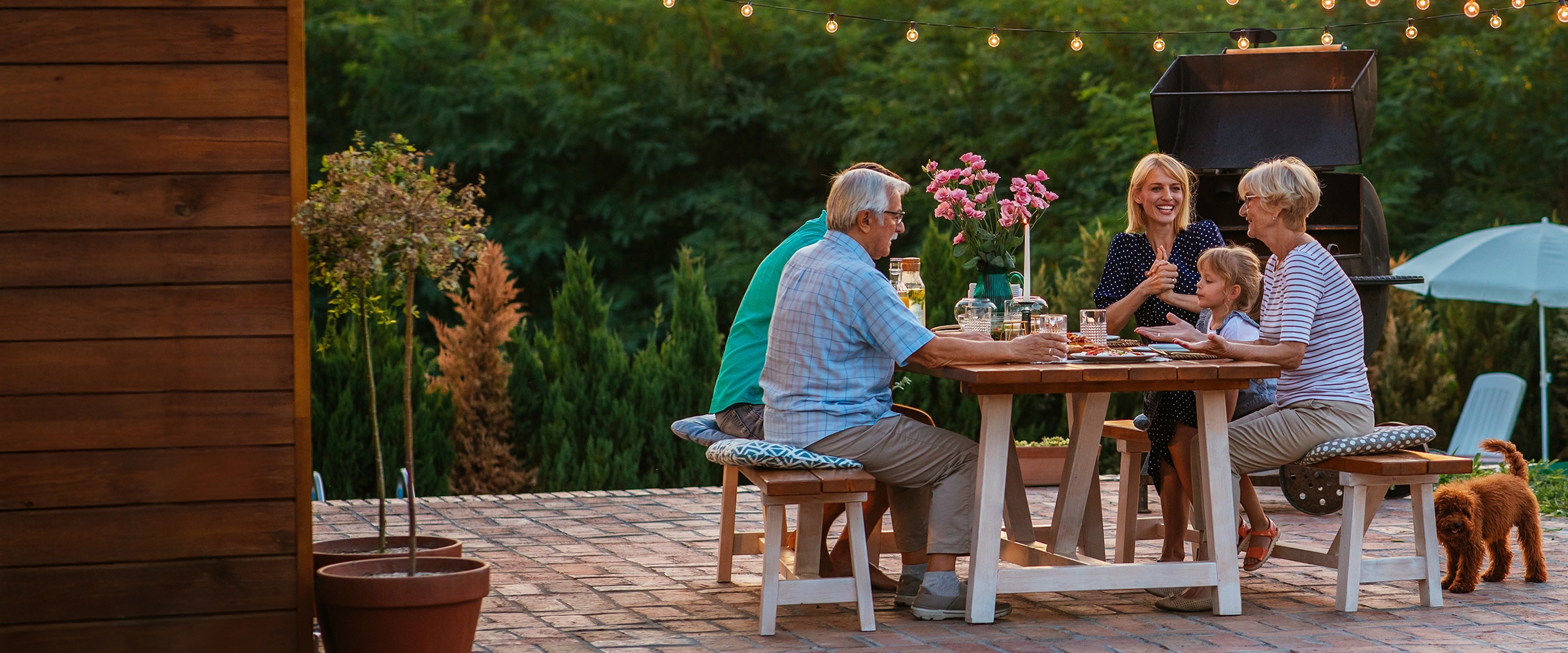 Photo of a young family and their parents sitting at a backyard table.
