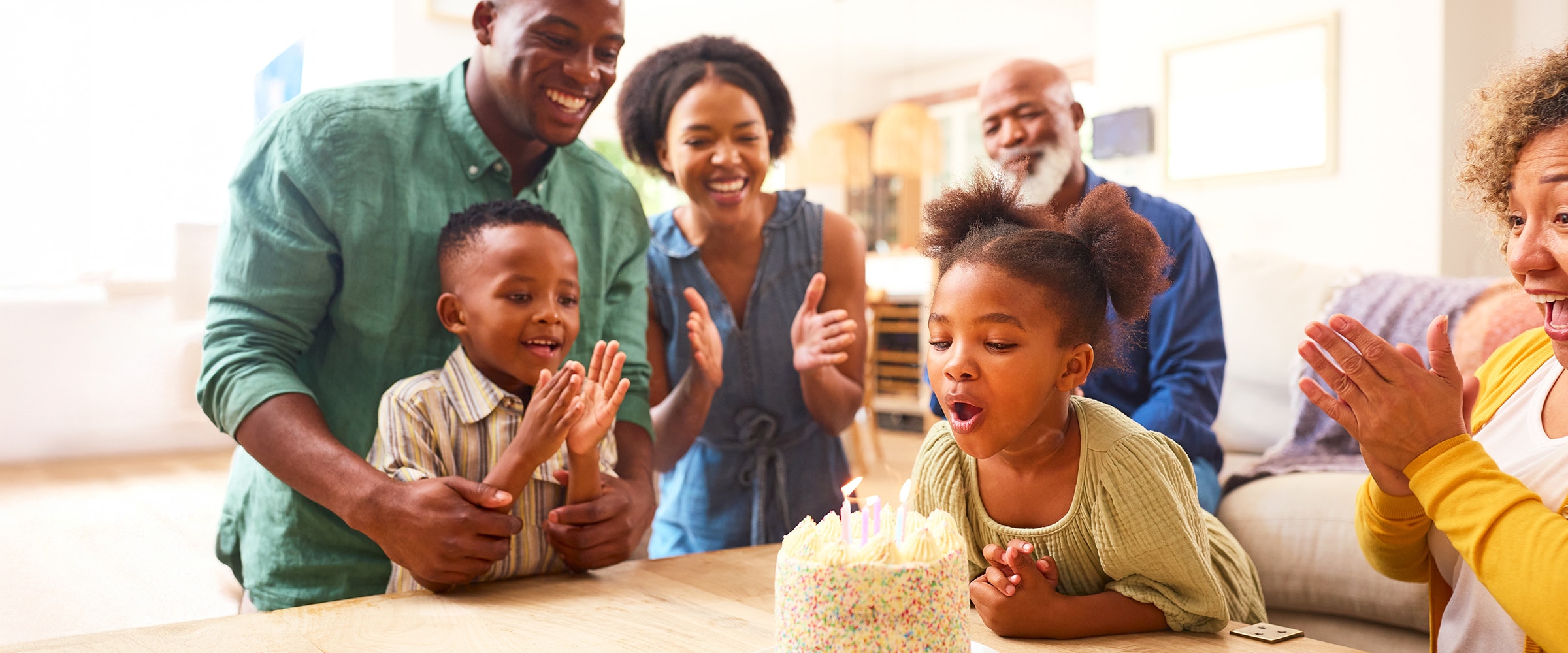 Photo of black family around young girl blowing out birthday candles.