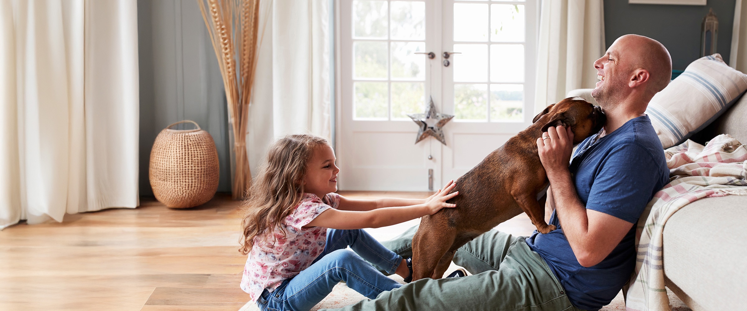 Photo of dad siting at the edge of a couch with a dog laying on top of him.