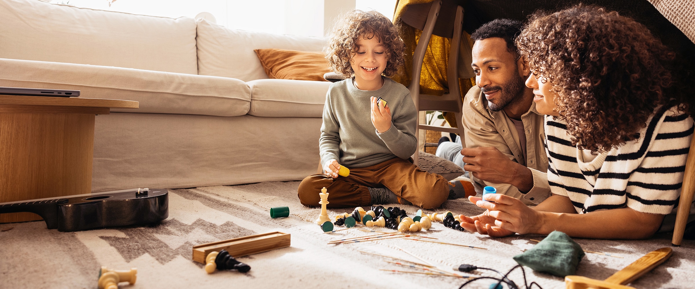 Photo of couple and child under a makeshift tent and playing a board game.