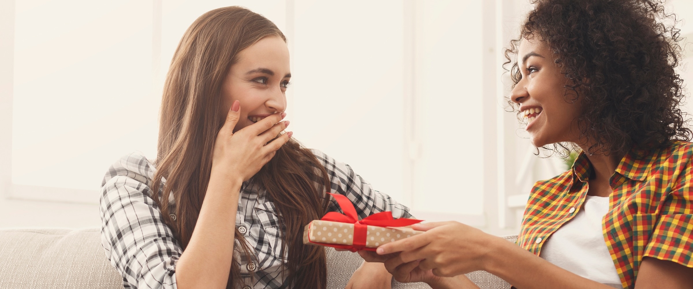 Photo of one woman giving another woman a red, bowed gift box.