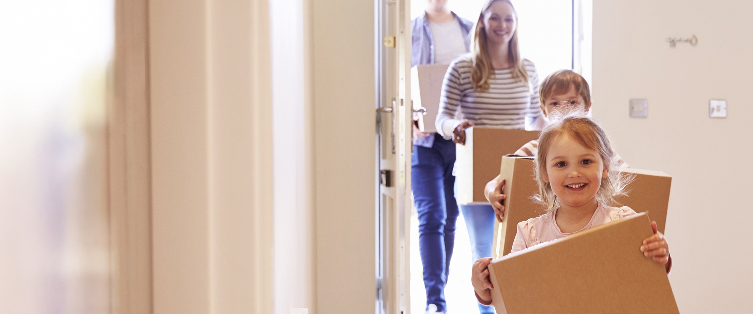 Photo of young family carrying moving boxes into new home.