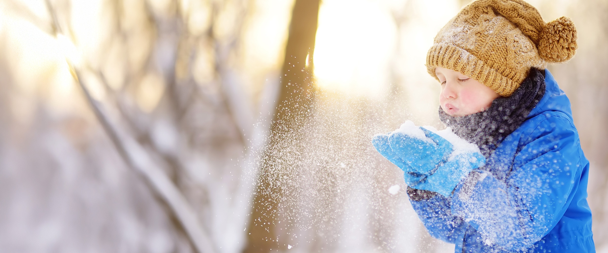 Photo of young child blowing snow from their mittens.