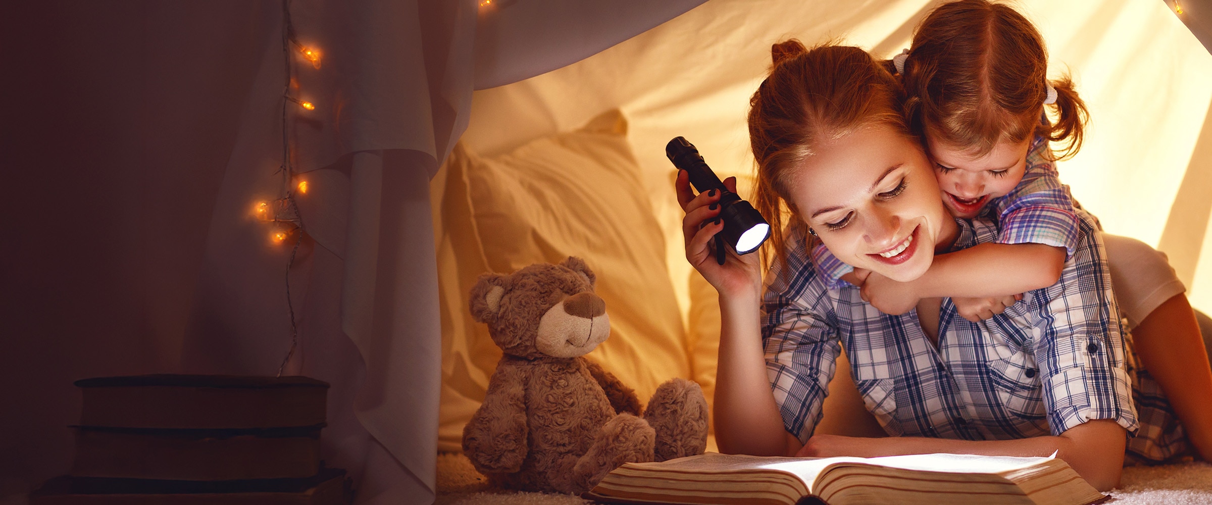 Photo of mom with flashlight reading with her child in a tent.