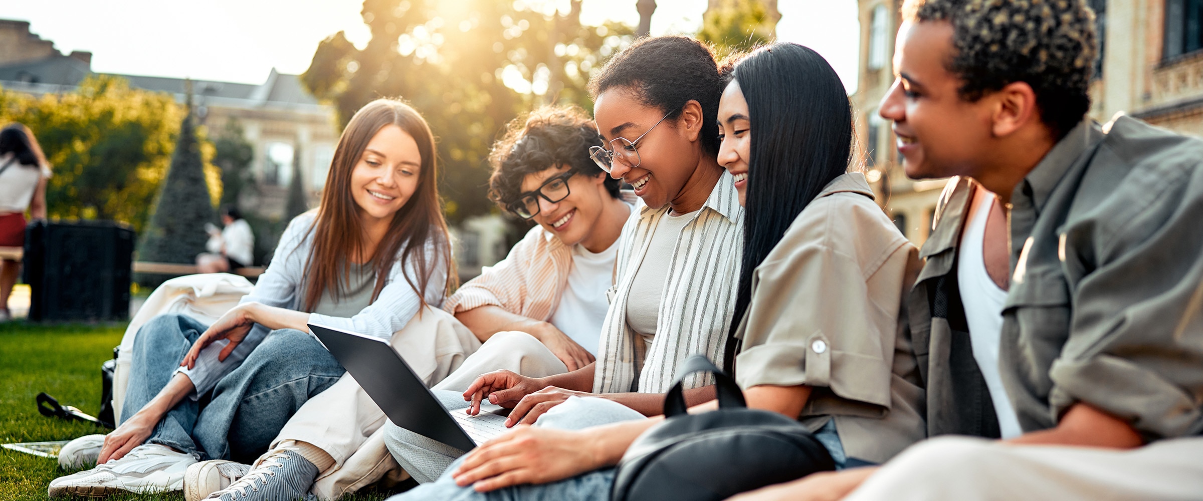 Photo of college kids sitting on campus quad looking at computer laptop.