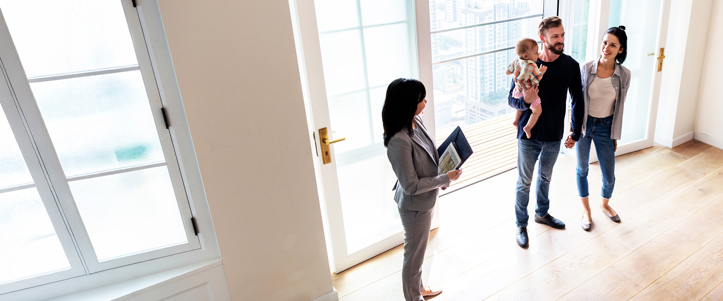 Photo of couple with child being shown the inside of a house by a realtor.ator