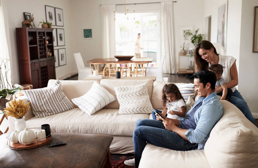 Family sitting on a  sectional in living room, engaging with tablet.