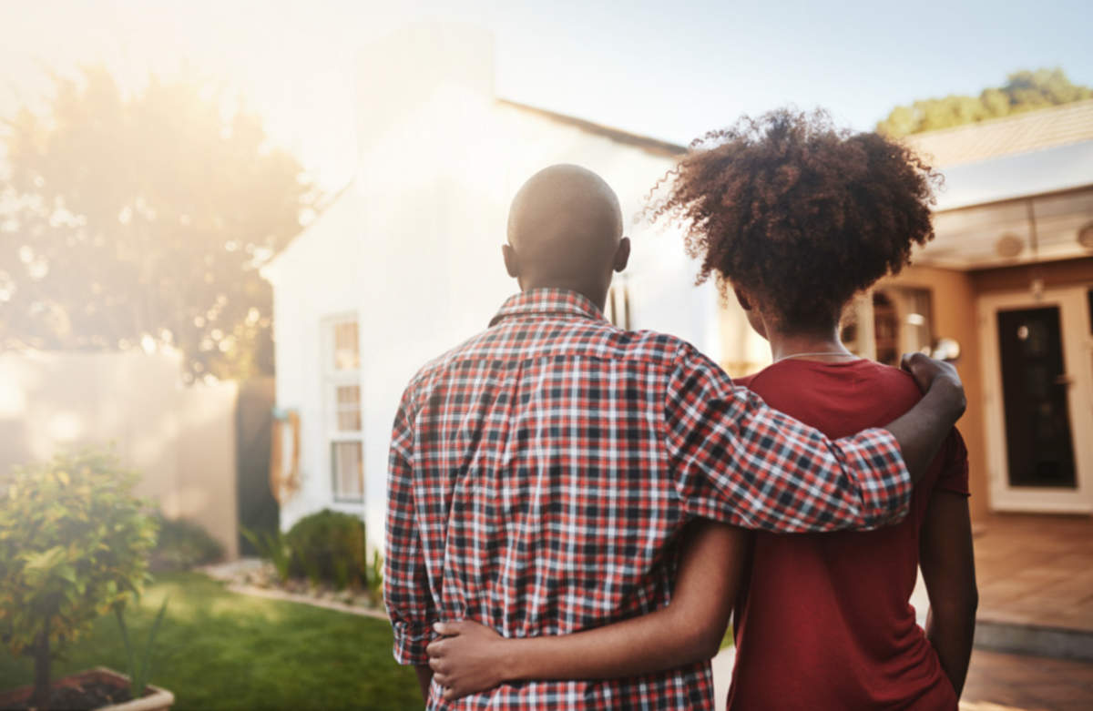Couple standing with arms around each other viewed from behind as they admire their home.