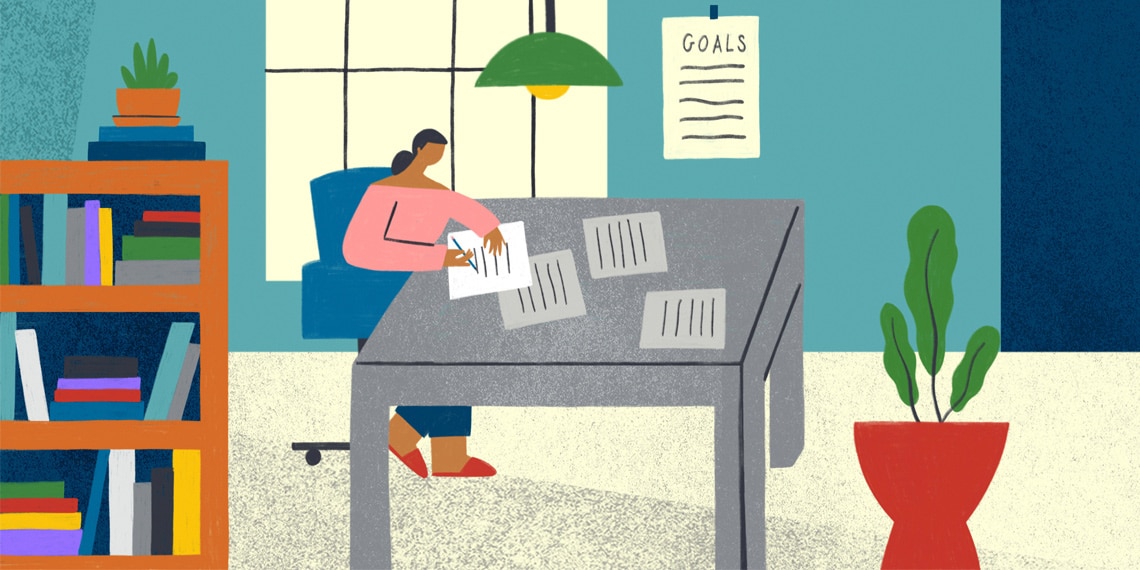 A woman writing at her desk, her goals can be seen pinned to wall.