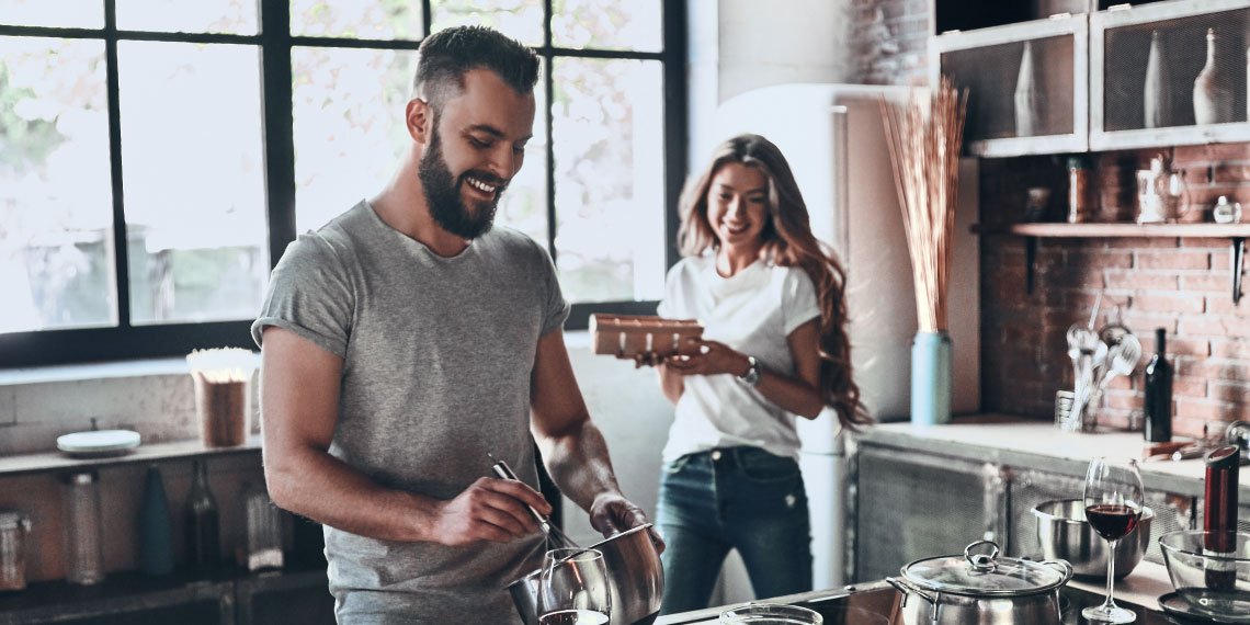Photo of younger couple preparing a meal in a kitchen.